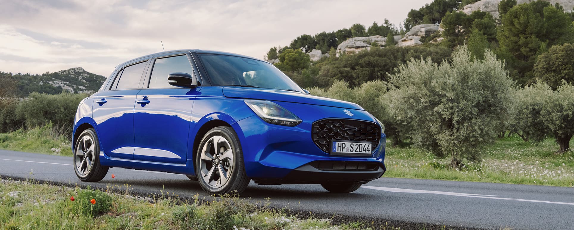 Ein blauer Suzuki Swift fährt dynamisch auf einer Landstraße