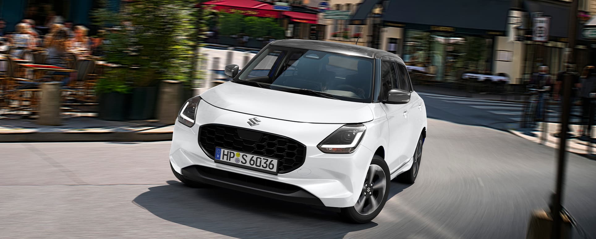 Ein weißer Suzuki Swift fährt in städtischer Umgebung dynamisch um eine Kurve