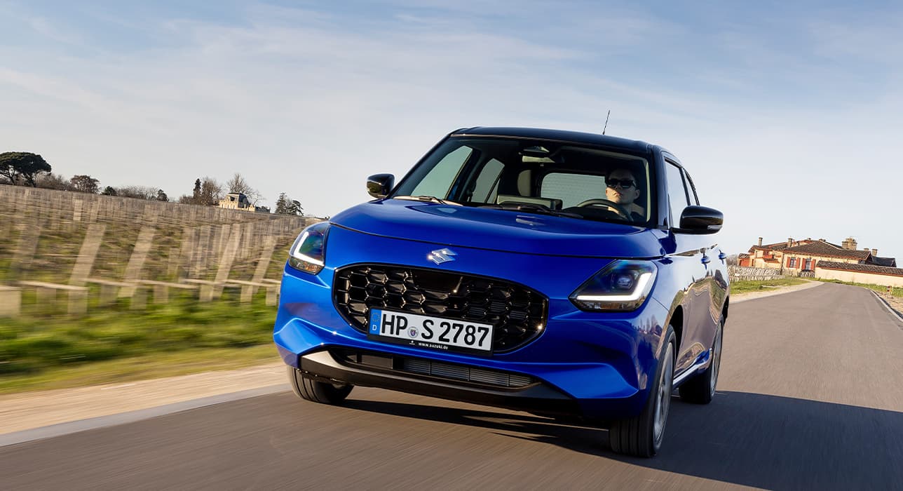 Blauer Swift fährt dynamisch auf einer Landstraße