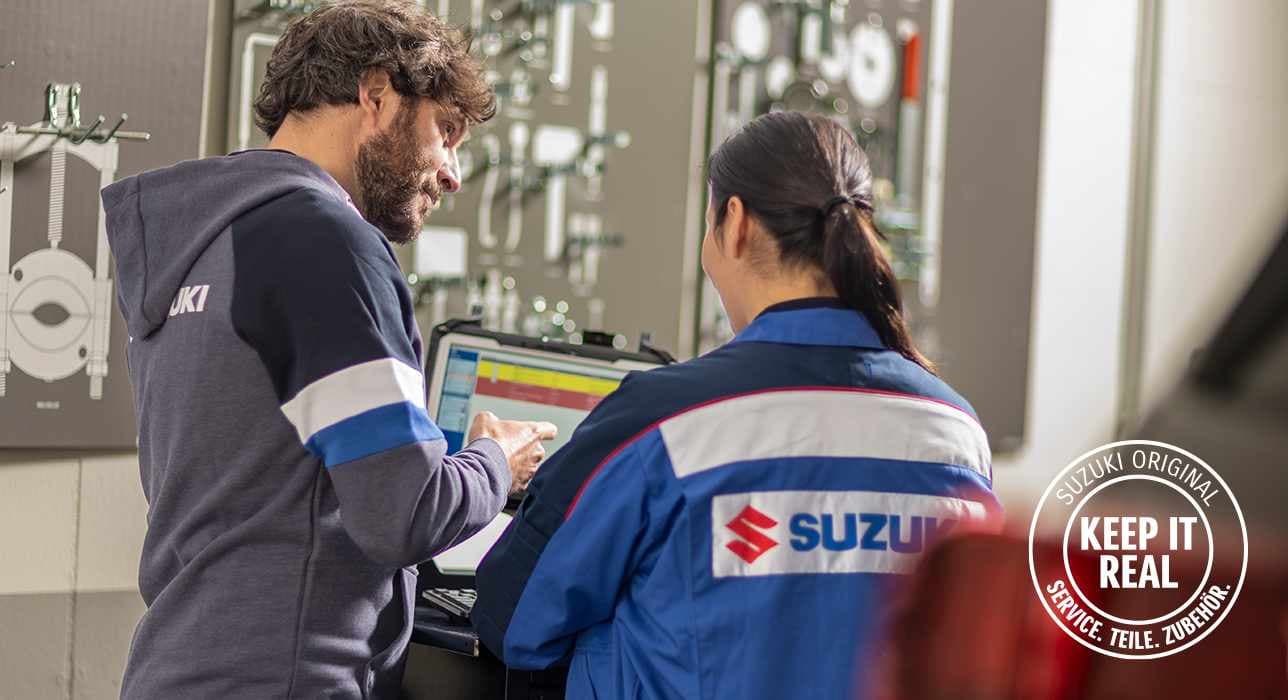 Abbildung zeigt zwei Mitarbeiter einer Suzuki werkstatt, einen Mann und eine Frau, die auf einen Diagnosebildschirm schauen.