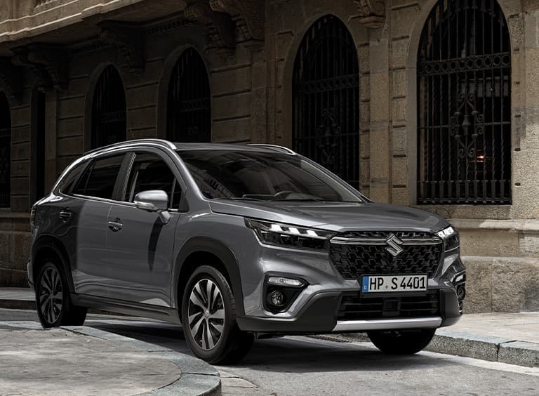 Abbildung zeigt einen S-Cross auf einer Straße vor einem Haus.