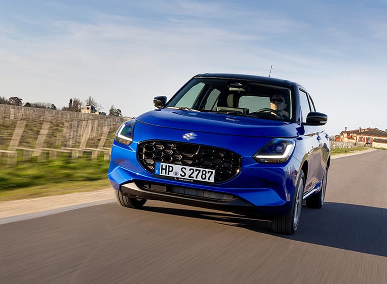 Blauer Swift fährt dynamisch auf einer Landstraße