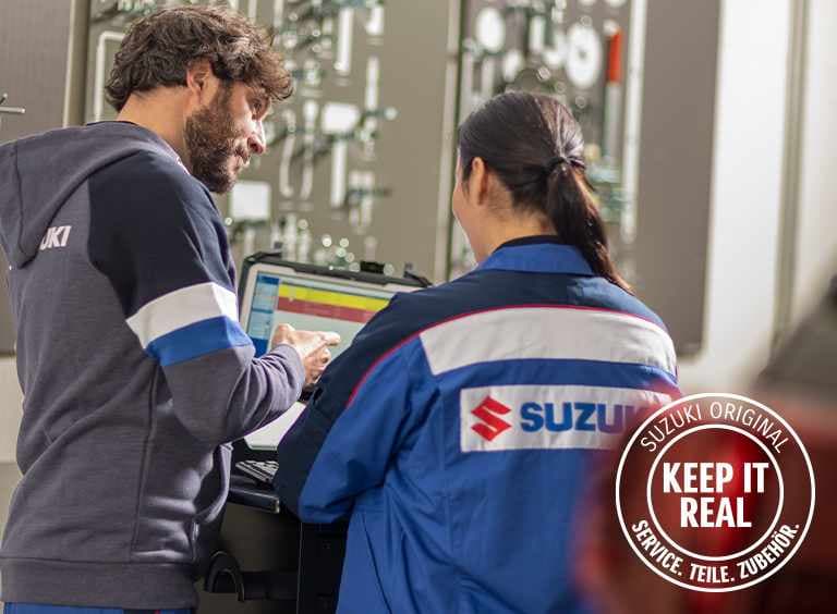 Abbildung zeigt zwei Mitarbeiter einer Suzuki werkstatt, einen Mann und eine Frau, die auf einen Diagnosebildschirm schauen.