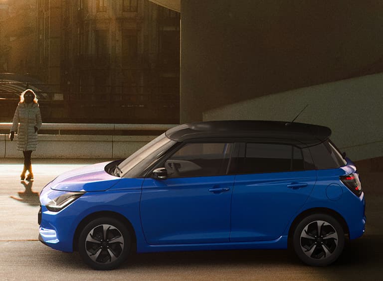 Abbildung zeigt blauen Swift mit UV & IR absorbierende Scheiben, der an einer Straße parkt und zwei Personen daneben spazieren gehen