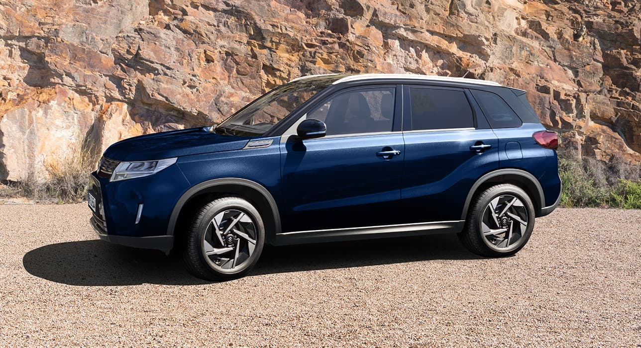 Abbildung zeigt blauen Vitara vor einem Hügel stehend